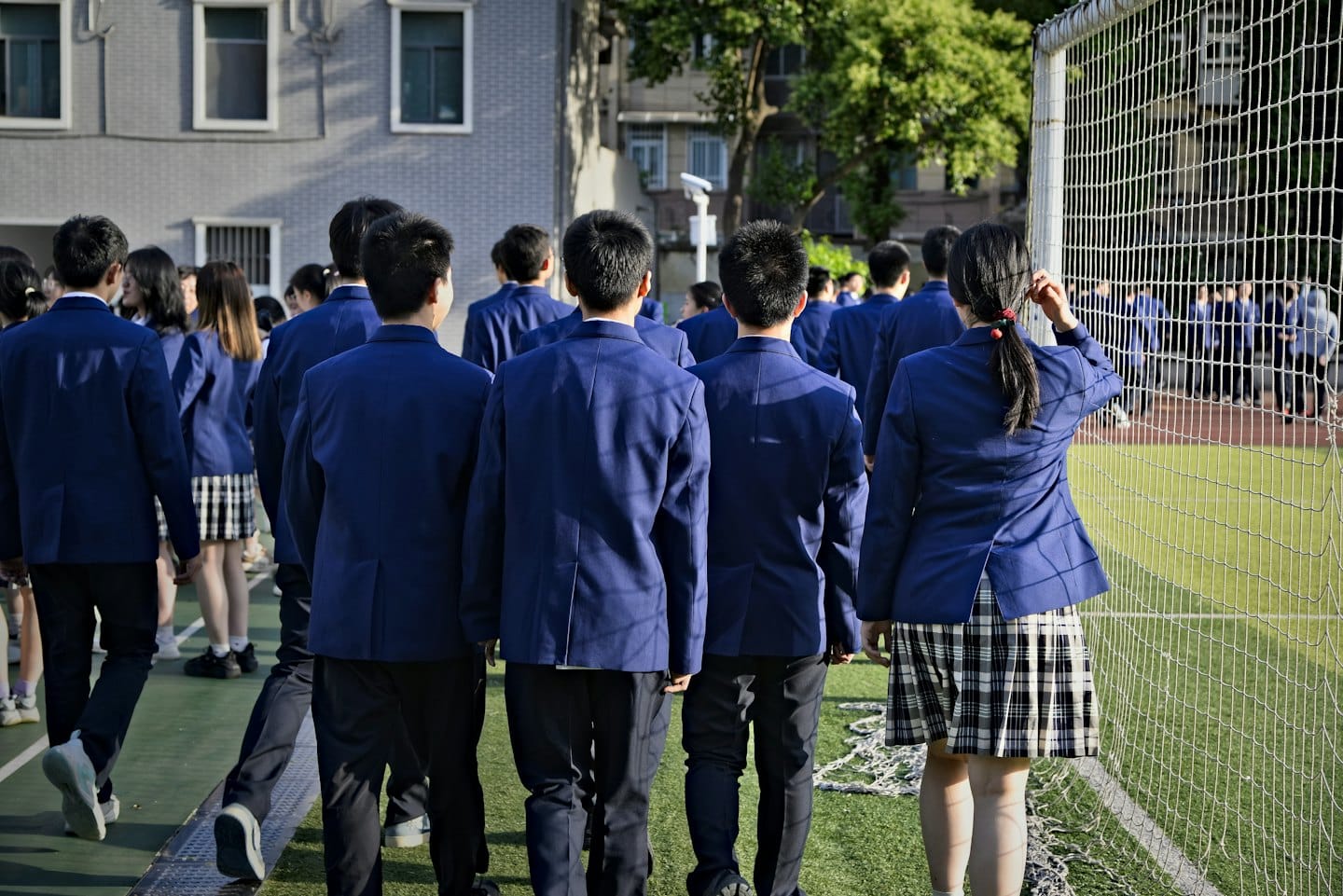 Students in school uniforms walk across a green field.