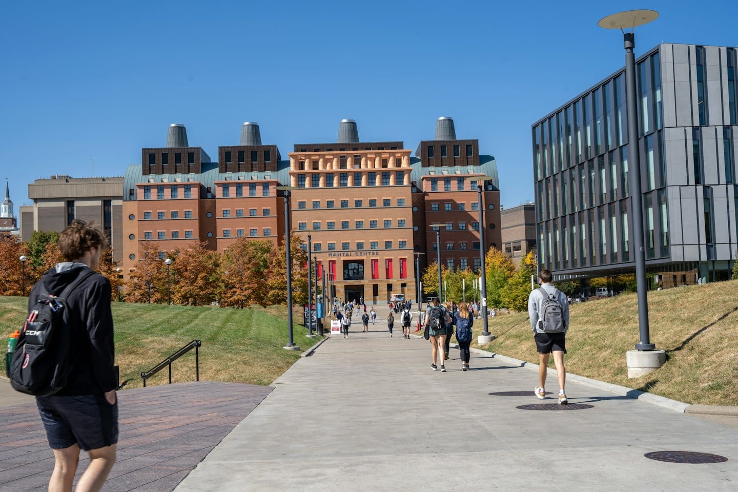 Students walk on a campus path towards a brick building.